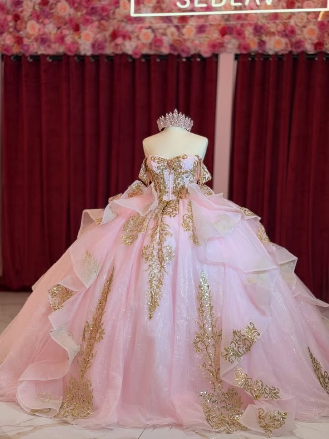 A blush quinceañera gown with gold embroidery, finished with a crystal tiara